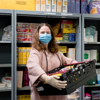 Foto van een vrouwelijke vrijwilliger met mondkapje op die een voedselpakket vasthoudt in de Voedselbank